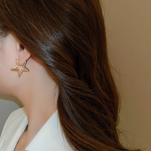 Close-up of elegant gold star-shaped hollow earrings worn by a model in warm lighting