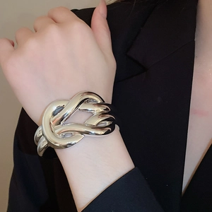 Detail of silver metallic knot bangle with polished mirror finish on model sleeve