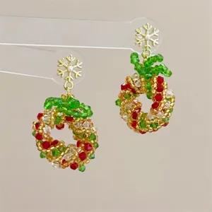 Macro detail of handmade beaded Christmas wreath earrings with gold snowflake studs
