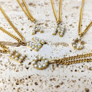 Close-up of gold stainless steel initial pendants with inlaid pearls on stone surface