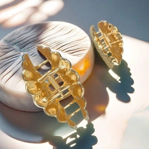 Detail of two gold metal shell hair claws on ceramic base with natural light shadows