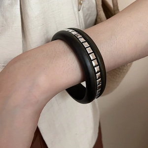 Détail d'un bracelet en bois noir avec des clous carrés argentés sur un poignet femme
