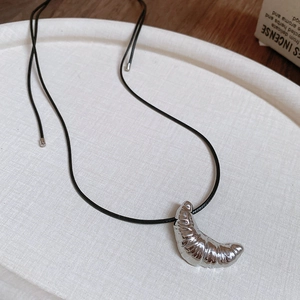 Detail shot of a silver croissant pendant necklace with black cord on a white tray