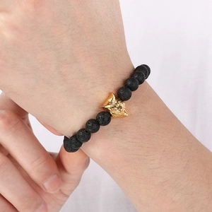 Close-up of black lava stone bracelet with a golden wolf head bead on a wrist