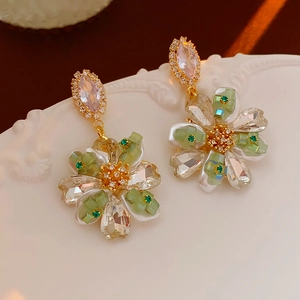 Détail de boucles d'oreilles fleurs avec cristaux verts et diamants sur céramique