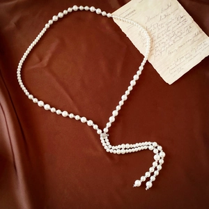 Detail of elegant long pearl necklace with diamond tassel on silk background