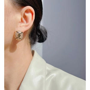 Détail d'une boucle d'oreille ronde dorée avec cristaux blancs et motif en émail noir