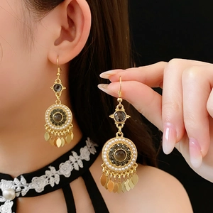 Détail de boucles d'oreilles vintage dorées avec gemmes noires, perles et feuilles