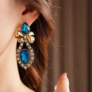 Close-up of vintage gold bow earrings with blue teardrop crystals and sparkling rhinestones