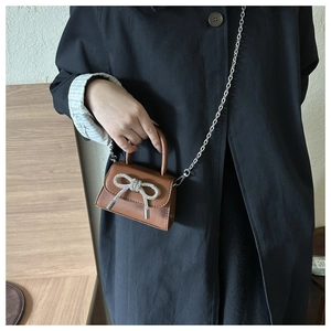 Detail of dark brown mini bag with sparkling bow buckle and silver chain strap