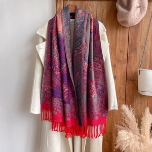 Close-up of ethnic paisley pattern scarf with fringes in red and gold on a white coat