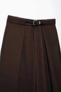 Détail du pantalon marron foncé avec fine ceinture noire et taille plissée