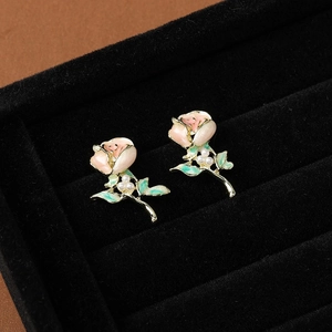 Macro shot of pink enamel rose earrings with green leaves and pearls on black velvet