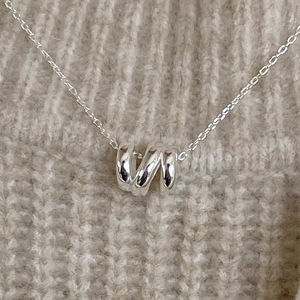 Polished silver spiral pendant necklace displayed on a beige knitted sweater background