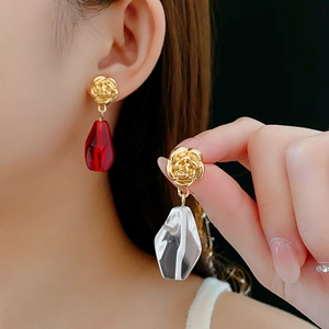 Detail of floral gold earrings with asymmetric red and clear faceted glass pendants