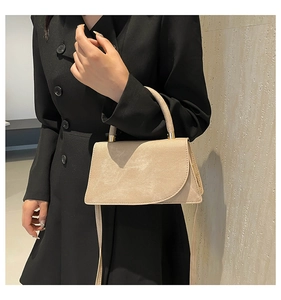 Detail of beige crossbody bag with curved flap and gold metal clasp on black coat