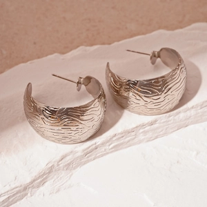 Macro detail of silver C-shape earrings featuring an intricate wavy embossed texture