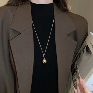 Close-up of a minimalist golden ball pendant necklace worn with a stylish blazer