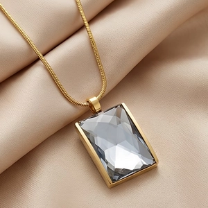 Macro detail of 18K gold plated snake chain with grey emerald cut glass pendant on satin