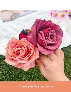 Close-up of pink and burgundy fabric rose hair claws held against a green grass background
