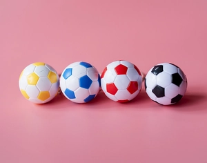 Vue à plat de quatre mini porte-clés de football colorés sur un fond rose vif