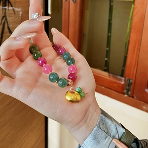 Detail of pink and emerald beads bracelet with a golden Fu character charm