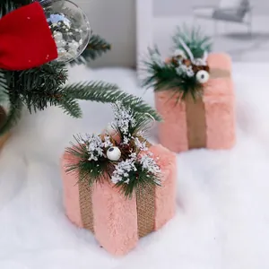 Pink plush Christmas gift box decor with pine needles and cones on white fur rug