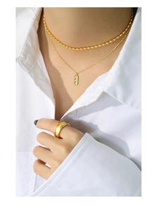 Detail of layered gold necklaces with zircon pendant and textured wide ring on model