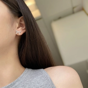 Close-up of a silver bow earring with pavé zircon stones worn by a model in soft light