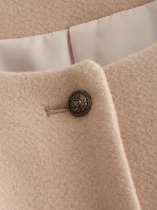 Macro detail of apricot wool jacket showing textured fabric and vintage crest metal button
