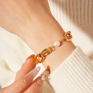Close-up of gold plated chunky chain bracelet with freshwater pearl on a knit sleeve