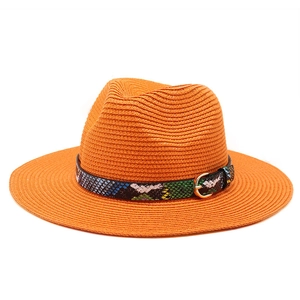 Macro shot of orange straw fedora with snake print band and golden metal buckle details