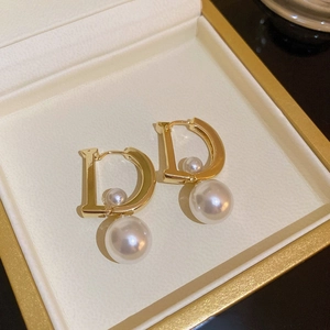 Detailed close-up of D-shaped earrings with pearls in a luxury beige jewelry box