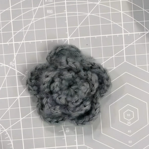 Detail of a 7cm grey triple-layered crochet flower showing yarn texture on a cutting mat