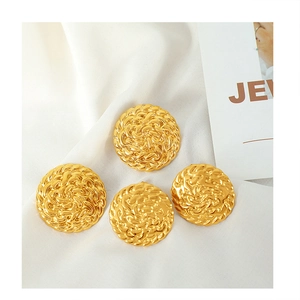 Detailed close-up of vintage gold round earrings with woven texture on white silk fabric
