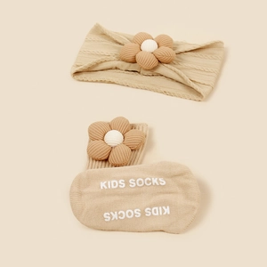 Détail d'un bandeau tricoté pour bébé avec fleur en tissu et chaussettes antidérapantes