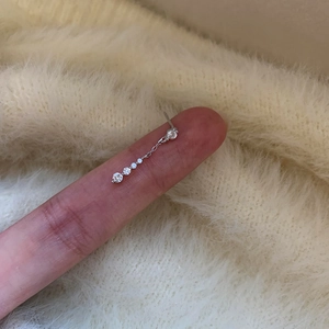 Macro detail showing a silver needle zircon drop earring on a finger for scale