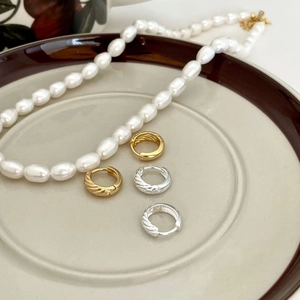 Elegant twisted rope hoop earrings in gold and silver finish on a ceramic tray