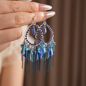 Dettaglio di orecchini boho con cristalli blu, zirconi e nappe metalliche in stile etnico