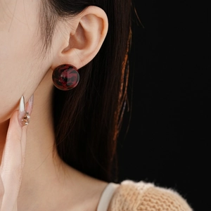 Close-up of a model wearing round leopard print earrings with dark red marble resin finish