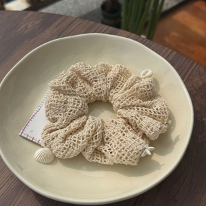 Close-up of cream linen knit hair scrunchie with shell pendant on ceramic plate
