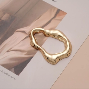 Irregular gold wave buckle with liquid metal texture on fashion magazine background