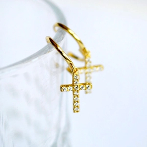 Detail of gold cross hoop earrings with white zircon hanging on a glass rim