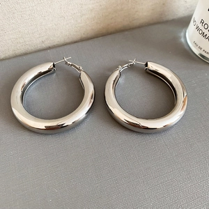Close-up of large polished silver hoop earrings on a textured background