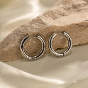 Minimalist silver stainless steel hoop earrings displayed on silk and natural stone