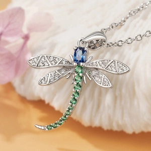 Exquisite silver dragonfly pendant necklace with blue and green gemstones on plush background