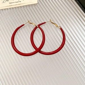 Macro shot of red enamel hoop earrings with gold clasp on a striped white surface