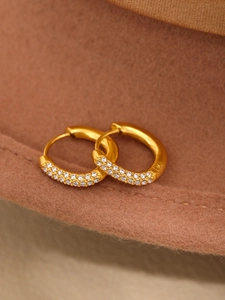 Macro shot of gold hoop earrings with sparkling white cubic zirconia on brown fabric