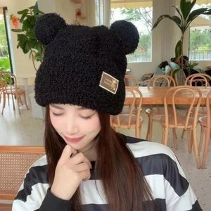 Close-up of black fuzzy winter hat with bear ears and metallic logo label detail