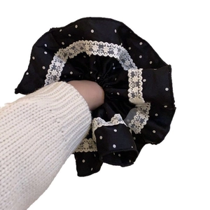 Retro black polka dot satin scrunchie with white lace trim on model's wrist